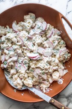 a bowl full of potato salad on top of a marble table with a wooden spoon