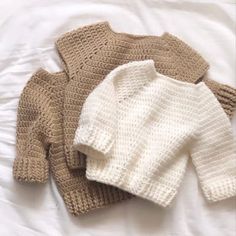 two knitted sweaters laying on top of a white bed next to each other