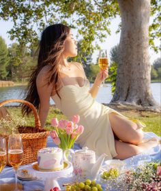 a woman sitting on a blanket holding a glass of wine in front of a picnic table