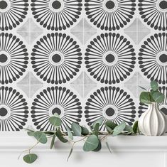 a white vase sitting on top of a mantle next to a wall with black and white tiles