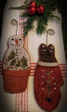 two knitted christmas stockings hanging from hooks on a tablecloth with evergreen needles and red baubles