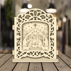 a laser cut nativity scene with the birth of jesus in white on top of a wooden table