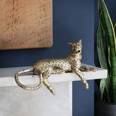 a cat figurine sitting on top of a white shelf next to a potted plant