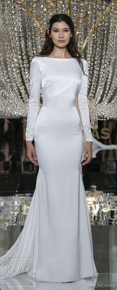 a model walks the runway in a white gown with long sleeves and an open back