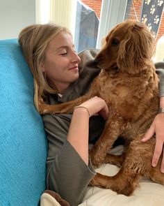 a woman sitting on a couch holding a dog in her lap and petting it