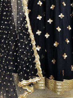 This stunning hand embellished gold mirror work blouse is teamed with a gorgeous black gold skirt with 3D sequins flower and gold border. This outfit is completed with a black scallop dupatta with scattered gold butis. Bollywood Style Gold Embellished Sharara, Embellished Black Sharara For Eid, Black Embellished Sharara For Diwali, Gold Embellished Anarkali Sharara, Elegant Black Salwar Kameez With Gota Work, Black Traditional Wear With Sequins, Gold Sequined Choli With Traditional Drape, Traditional Drape Gold Sharara With Sequins, Gold Sequined Traditional Sharara