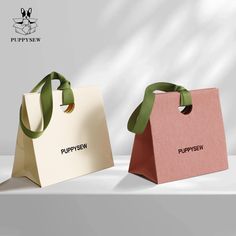 two paper bags with green ribbons on them sitting side by side in front of a white background