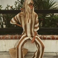 a woman sitting on a bench wearing a brown and white checkered jumpsuits