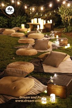 an outdoor lounge area with pillows and candles on the grass, surrounded by lights in the background