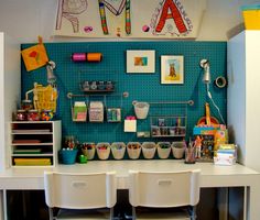 there is a desk with two white chairs and several storage bins on the wall