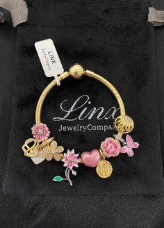 a gold bracelet with pink and white flowers on it, sitting in a black velvet bag