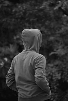 black and white photograph of a person in a hoodie looking at the trees outside