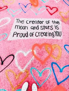 someone standing on the ground with their feet up in front of chalk hearts and a sign that says, the creator of the moon and stars is proud of creating you