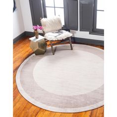 a round rug in the middle of a living room with a chair and window behind it