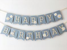 two happy birthday banners with daisies on blue and white paper, hanging from clothes pins