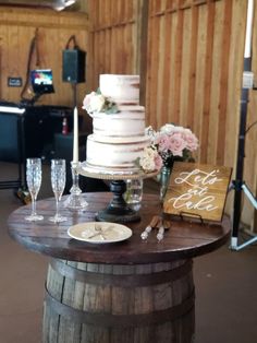 a wedding cake sitting on top of a wooden barrel next to wine glasses and flowers