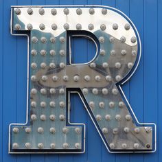 the letter r is made up of metal rivets on a blue building wall