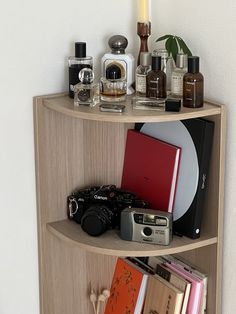 a corner shelf with books, cameras and other personal care items on it next to a white wall