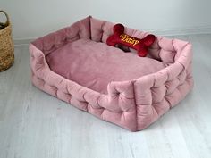 a pink dog bed with a red bone on it's side and a basket next to it