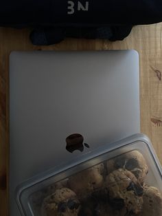 an open laptop computer sitting on top of a wooden table next to a plastic container filled with cookies