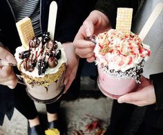 two people holding up ice cream sundaes with waffle cones and chocolate drizzle