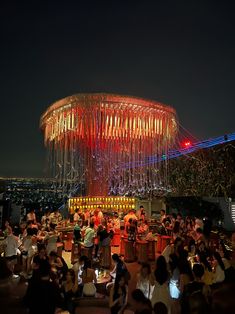 a large group of people sitting at tables in front of a lit up structure on top of a hill