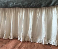 a bed with white ruffled bedspread on it's headboard and wooden flooring