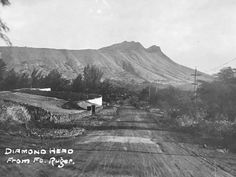 an old black and white photo of a dirt road with mountains in the back ground