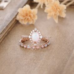 a white opal and diamond ring sitting on top of a wooden table next to flowers