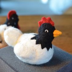 two small stuffed chickens sitting on top of a book with one laying down and the other standing up