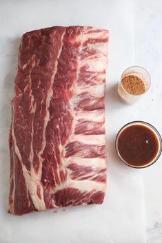 raw meat sitting on top of a cutting board next to sauces and seasoning