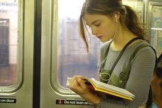 a young woman reading a book while riding the subway