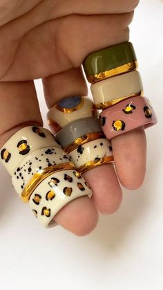 a hand holding five different colored rings on it's fingers with gold trims