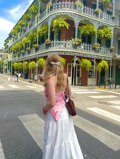 a woman in a white dress is standing on the side of the road looking at a building