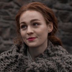 a woman with red hair is wearing a gray knitted scarf and looking at the camera