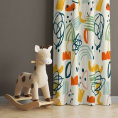 a wooden rocking horse in front of a curtain with an abstract design on it's side