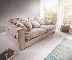 a couch sitting in front of a window next to a rug and book on the floor