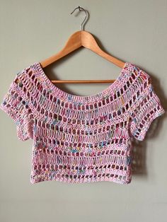 a pink crocheted top hanging on a wooden hanger next to a wall