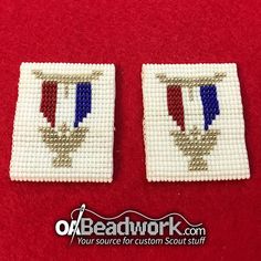 two cross stitched squares with red, white and blue designs on them sitting on a red surface