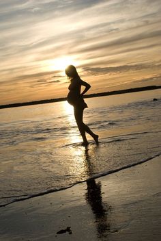 a woman is running on the beach at sunset with her arms behind her back and feet in the water