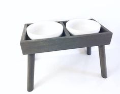 two white bowls sit on top of a small wooden stand that holds two smaller bowls