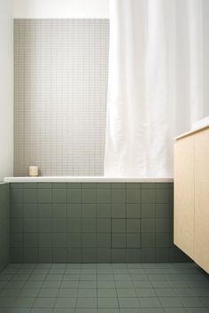 an empty bathroom with green tile and white shower curtain over the bathtub, in front of a window