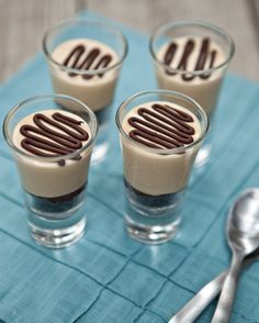 three glasses filled with dessert sitting on top of a blue napkin next to spoons