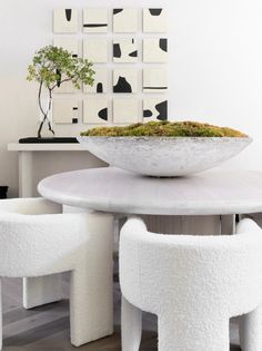 a bowl with moss sits on top of a table surrounded by white chairs and stools