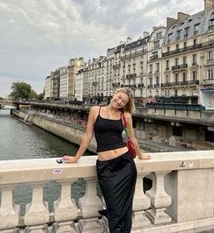 a woman standing on a bridge next to the water with buildings in the back ground