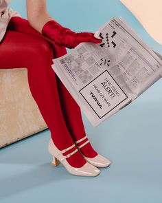 a woman in red stockings and white shoes is sitting on a bench reading a newspaper