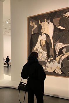 a woman standing in front of a painting on display at an art gallery with people walking by