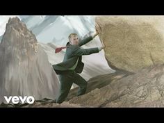 a man in a suit and tie standing on top of a mountain next to a giant rock