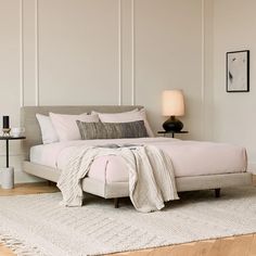 a white bed sitting on top of a wooden floor next to a night stand and lamp