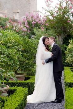 a bride and groom kissing in the middle of a garden with hedges, bushes and flowers